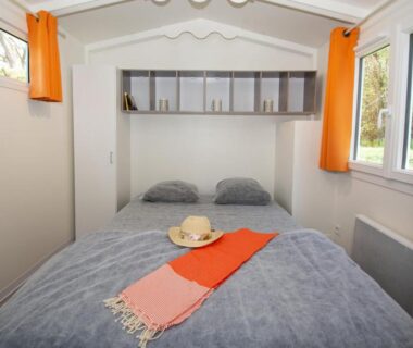 Intérieur chambre avec lit double et rideaux orange dans le mobil-home A La Rencontre Du Soleil Camping