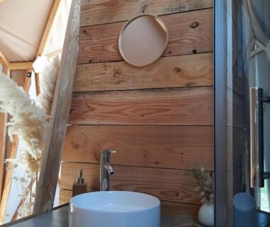 Dans la tente un lavabo en pierre sur meuble devant mur en bois du camping A l'aube des sens