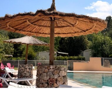 Bord de piscine avec parasols en paille et chaises longues à l'Aloha Camping Club