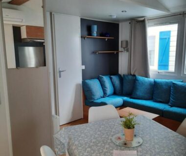 Intérieur du séjour avec canapé d'angle bleu et table à manger dans le mobil-home Aquapark -DESS