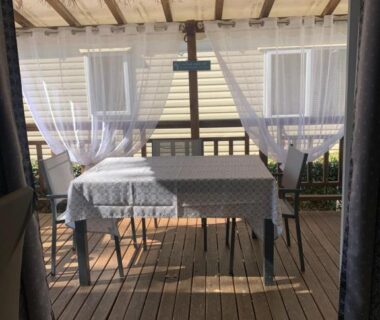 Terrasse couverte avec table et rideaux dans le camping Au Petit Bonheur