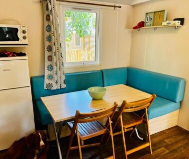 Coin repas intérieur avec banquette bleue table en bois et kitchenette dans l'hébergement Au cœur des Pins
