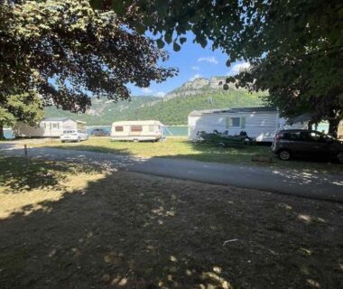 Emplacement ombragé avec caravanes et montagnes en arrière-plan au Bungalow camping Bel Air Village