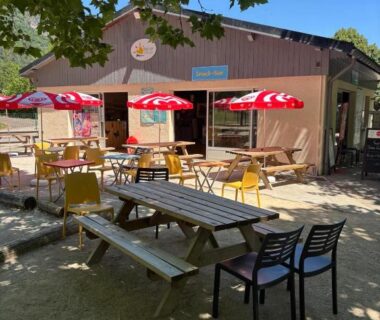 Terrasse ombragée avec tables chaises et parasols au bungalow du camping Bel Air Village