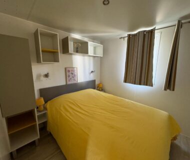 Chambre avec lit double et couette jaune dans le Bungalow les Embruns