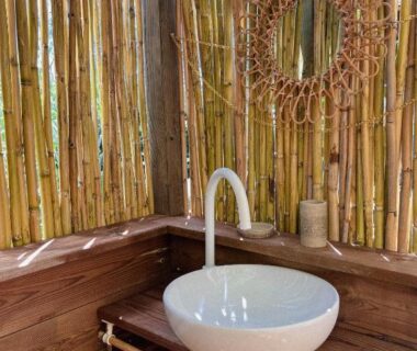 Coin lavabo en bois avec vasque blanche et miroir en rotin au Camping Gallina Varja