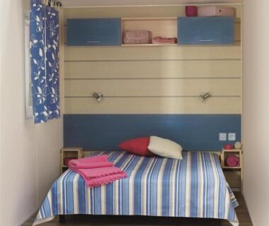 Chambre avec lit rayé et serviettes pliées au CAMPING LES EMBRUNS 3*