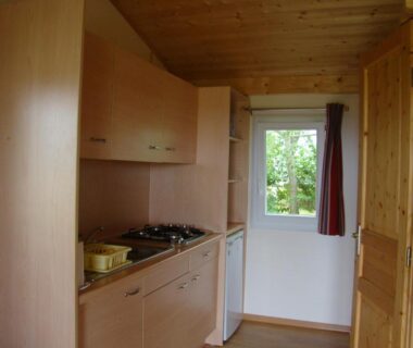 Intérieur kitchenette en bois avec plaque et fenêtre au Camping Les Graves