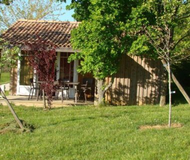 Pelouse et chalet en bois sous arbres au camping Les Graves