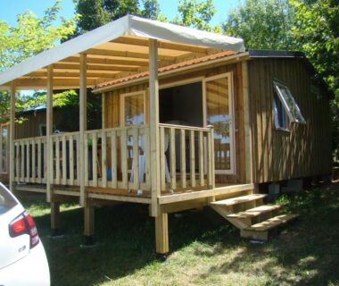 Devant la végétation cabane en bois sur pilotis avec terrasse au Camping Les Graves Cabane TITHOME