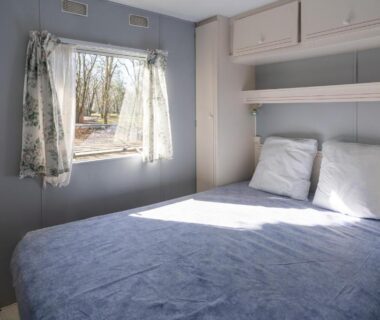 Intérieur de mobilhome avec lit double et fenêtre au Camping Les Paillotes