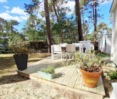 Terrasse en bois avec table et pots sous les pins au camping Les EMBRUNS