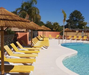 Piscine extérieure bordée de transats jaunes et parasols en paille au CAMPING RÊVE DES ILES
