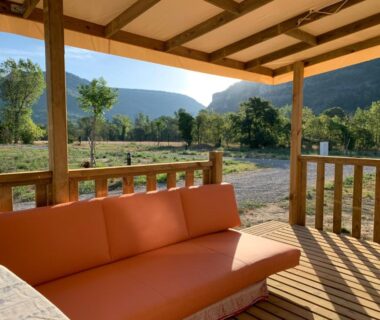 Terrasse en bois avec canapé orange et vue sur la vallée du camping Calme & Sérénité