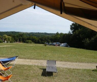 Prairie et emplacements avec chaises et transat vus depuis une tente au Camping 3 étoiles Piscine chauffée Périgord Vert