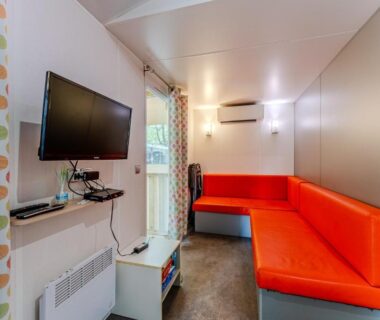 Intérieur avec banquette orange et télévision au Camping 4 étoiles parc aquatique