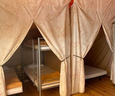 Intérieur de tente avec lits superposés et rideaux au Camping 46 Rainettes