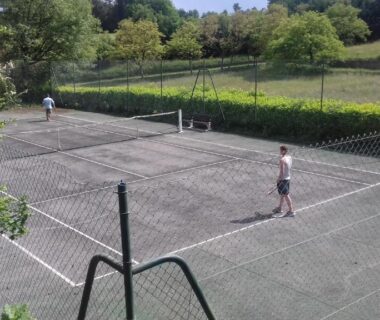 Terrain de tennis extérieur entouré d'arbres au Camping 46 Rainettes