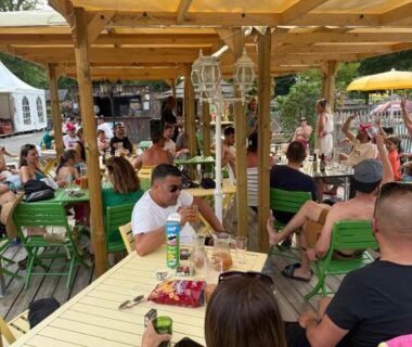 Terrasse sous pergola en bois avec tables et convives au camping A l'Ombre des Tilleuls