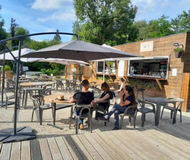 Terrasse avec tables parasols et snack en bois au Camping Aqua Viva