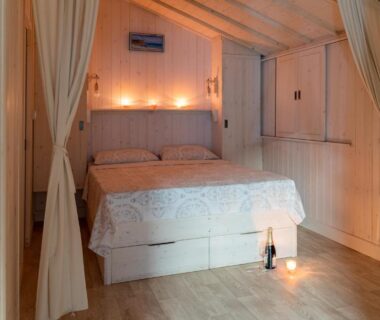 Chambre en bois avec lit double bougies et bouteille au Camping Arutoli