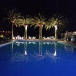 Piscine éclairée la nuit avec palmiers et chaises longues au Camping Arutoli