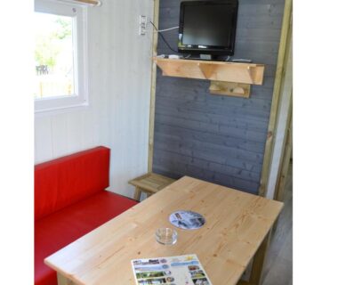 Coin repas avec banquette rouge et télévision dans le logement du Camping Au Lac d'Hautibus