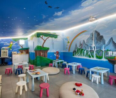 Salle de jeux enfants avec fresque murale et tables au Camping Bel Air
