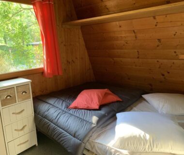 Chambre en bois avec lits et rideau rouge dans un chalet du Camping Calme et Nature Iserand