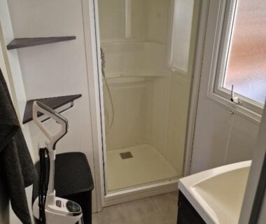 Salle d'eau avec cabine de douche lavabo étagères et aspirateur dans le Camping Carabasse Vias plage