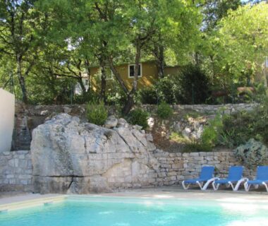 Piscine extérieure bordée de rochers et transats au Camping Chalets Les Chênes Verts