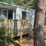 Mobil-home sur terrasse en bois avec chaises parmi les pins au Camping Cœur De Vendée