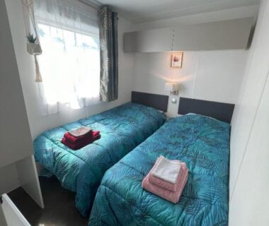 Chambre avec deux lits simples serviettes pliées et fenêtre dans le Mobile Home O'Hara Supérieur 1060