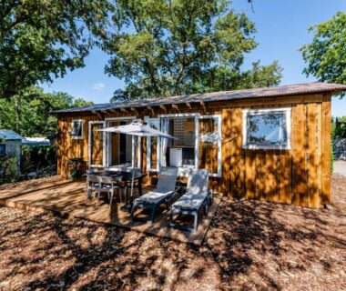 Terrasse en bois avec transats et parasol sous arbres du Camping Domaine Les Oréades – Maeva Sélection