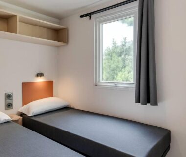 Chambre avec deux lits simples et fenêtre du mobile-home pour 6 personnes au Camping Domaine la Yole