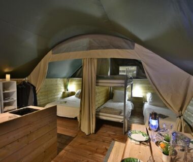 Intérieur de tente avec lits superposés coin repas et éclairage chaleureux au Camping Du Paquier Fané