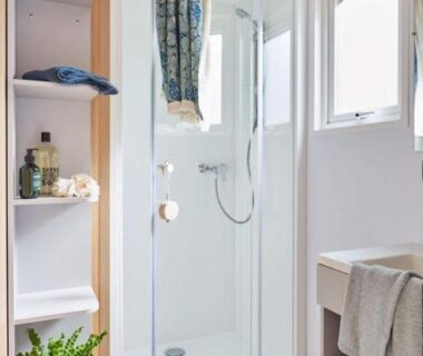 Salle de bain avec cabine de douche vitrée étagères et serviettes du Camping Du Paquier Fané