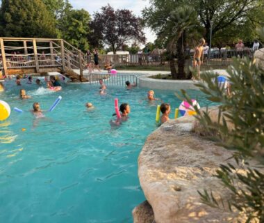 Piscine extérieure avec baigneurs et pont en bois au Camping Dun-le-Palestel