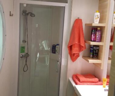 Salle de bain avec cabine de douche lavabo étagères et serviettes au Camping Eden