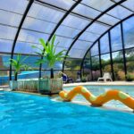 Piscine couverte avec toboggan, plantes et transats au Camping Etennemare