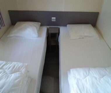 Chambre de mobil-home avec deux lits simples séparés par une table de chevet au Camping Figurotta