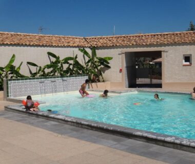 Piscine extérieure avec enfants et bananiers en arrière plan au Camping Hameau Des Cannisses