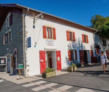 Façade du bâtiment d'accueil avec volets rouges et visiteurs du Camping Harrobia