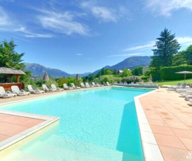 Piscine extérieure et transats avec montagnes en arrière plan au Camping-Hotel de Plein Air Les 2 Bois