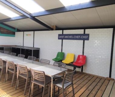 Salle couverte avec grande table et chaises au Camping Insolite Le Haut Village