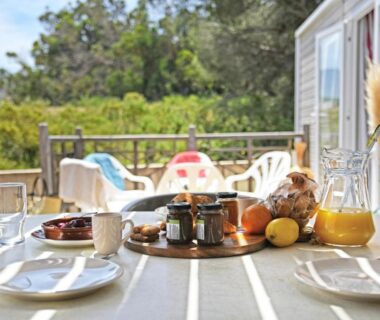 Terrasse avec table dressée, tasses et pain dans un cadre verdoyant au Camping International