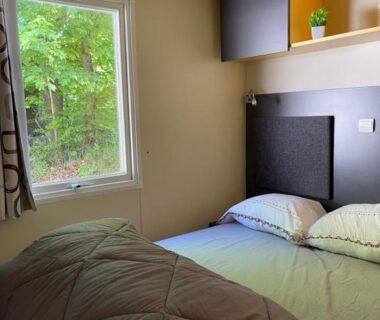 Chambre avec lit double et fenêtre sur la végétation au Camping L Eden Road