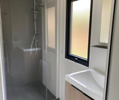 Salle de bain avec douche vitrée lavabo et fenêtre dans le mobile home du Camping LE MOULIN DE CAUDON
