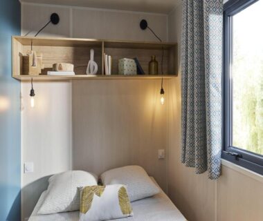 Intérieur de mobil-home avec lit coussins et étagères au Camping LE MOULIN DE CAUDON