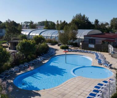 Piscine extérieure entourée de transats et d'abris vitrés au Camping L'Orée du Bois